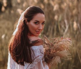 Young brunette women in a white blouse and long skirt with a bouquet of dried flowers in the middle of the field. The beauty of autumn nature